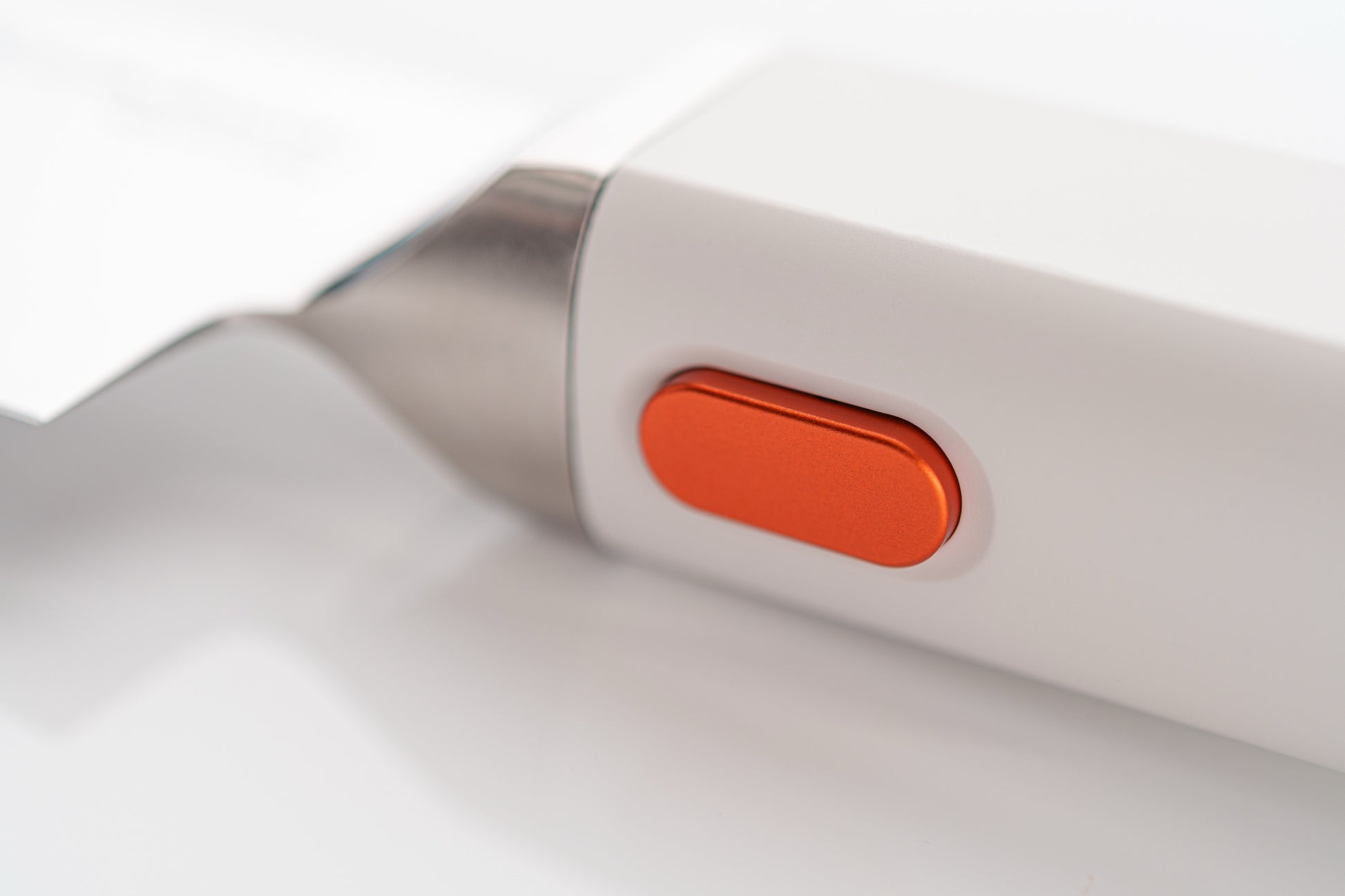 Close-up of a white electronic chef knife with an orange button on a light gray background